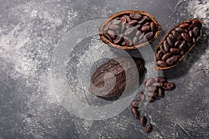 Split fermented cocoa pod with shelled cacao beans atop dark grey backdrop,  top view