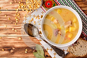 Split pea soup with meat, potatoes and carrots in ceramic bowl on wooden background.