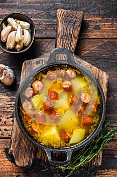 Split pea soup with smoked sausages in a pan. Dark wooden background. Top view
