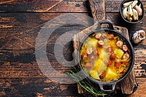 Split pea soup with smoked sausages in a pan. Dark wooden background. Top view. Copy space