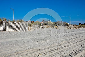 Split rail fence lining a pathway over sand dunes and high grass entering a white sandy beach