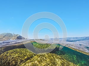 Split underwater view of a blue sky over a rocky shore in Alghero