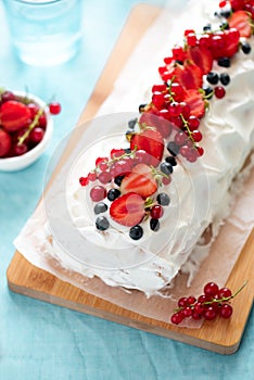 Sponge biscuit cake roll filling whipped cream and berries decorated strawberry, blueberry and red currants on turquoise