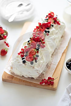 Sponge biscuit cake roll filling whipped cream and berries decorated strawberry, blueberry and red currants on white wooden