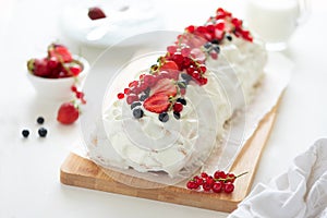 Sponge biscuit cake roll filling whipped cream and berries decorated strawberry, blueberry and red currants on white wooden