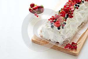 Sponge biscuit cake roll filling whipped cream and berries decorated strawberry, blueberry and red currants on white wooden