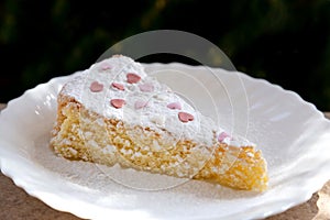 Sponge cake with cream and white chocolate decorate. Sliced piece of cake on white plate. Served on wooden table. Favorite dessert