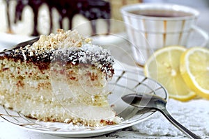 Sponge cake with creame coconut and chocolate. Behind a cup of tea with lemons