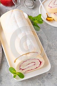 Sponge cake roll with strawberry jam and cream on a white plate on a gray background. Copy space