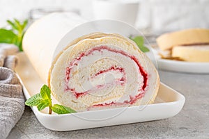 Sponge cake roll with strawberry jam and cream on a white plate on a gray background. Copy space