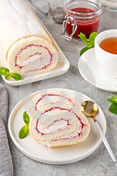 Sponge cake roll with strawberry jam and cream on a white plate on a gray background. Copy space