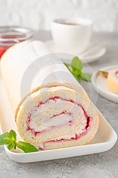 Sponge cake roll with strawberry jam and cream on a white plate on a gray background. Copy space