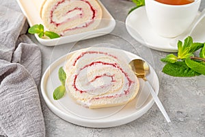 Sponge cake roll with strawberry jam and cream on a white plate on a gray background. Copy space