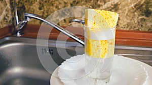 Sponge with foam for washing dishes in glass on the sink at the kitchen.
