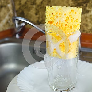 Sponge with foam for washing dishes in glass on the sink at the kitchen.