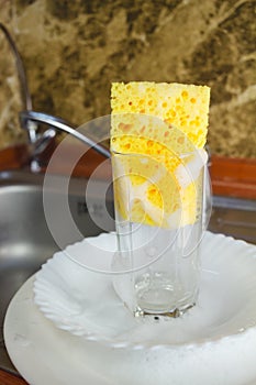 Sponge with foam for washing dishes in glass on the sink at the kitchen.