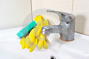 Sponge and gloves for washing dirty faucet with limescale, calcified water tap with lime scale on washbowl in bathroom, house