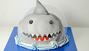 Sponge layered with frosting and raspberry jam, covered in soft icing with edible decorations, shark-shaped cake