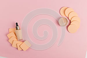 Sponges, a beautiful blender for applying foundation or powder and a bottle of concealer. Flat lay on a pink background, copy