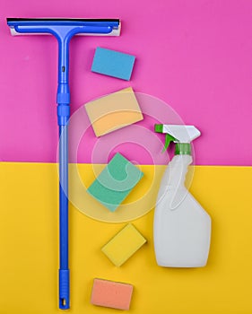 Sponges, window mop, sprinkler cleanser on a pink yellow background. Objects for home cleanliness. Products for cleaning