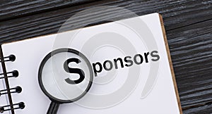 SPONSORS word written in a notebook on a dark beautiful background with a magnifying glass