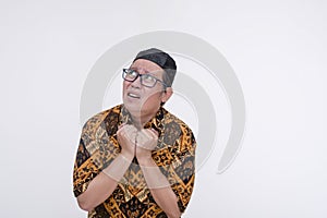 A spooked southeast asian muslim man loos around clenching his collar in fear. Wearing a batik shirt and songkok skull cap with