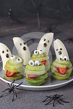 Spooky banana ghosts monsters and green kiwi monsters for Halloween party on brown background decorated with spiders and