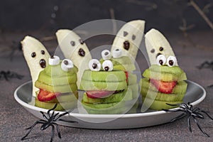 Spooky banana ghosts monsters and green kiwi monsters for Halloween party on brown background decorated with spiders and