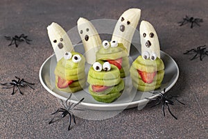 Spooky banana ghosts monsters and green kiwi monsters for Halloween party on brown background decorated with spiders