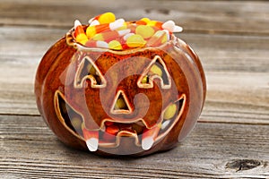 Spooky fanged pumpkin filled with candy corn on rustic wood