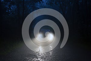 A spooky forest road with car headlights shining through the fog photo