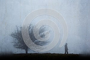 A spooky ghostly, silhouetted figure with glowing eyes next to a tree in winter. With a textured, weathered vintage edit