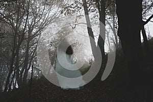 A spooky ghostly woman in a long white dress walking up a path through a moody misty autumn woodland