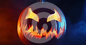 Spooky Halloween jack o lantern with glowing scary face carved out of a pumpkin and surrounded by smoke and mist