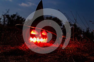 Spooky Halloween pumpkin jack-o-lantern in witch hat with burning candles in scary forest at night