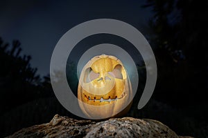 Spooky Halloween warm neon pumpkin in on a rock in the darkness