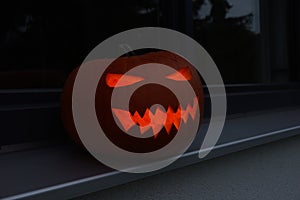 Spooky jack o`lantern standing on the window board of a home