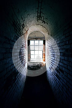 Spooky narrow old brick corridor with light shining through a window at the end