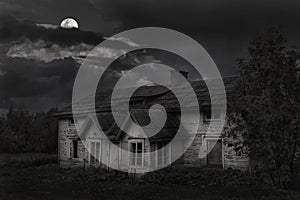 Spooky old house with bright moon and dark clouds at night with natural surroundings of trees and plants 