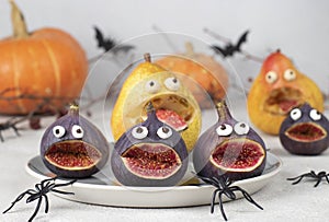 Spooky pear and fig monsters for Halloween party on gray background decorated with spiders and bats, Halloween Fruit