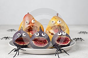 Spooky pear and fig monsters for Halloween party on gray background decorated with spiders, Halloween Fruit Serving Idea