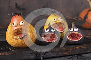 Spooky pear and fig monsters for Halloween party on wooden board decorated with spiders and bats, Halloween Fruit