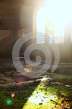 Spooky shot of chair in overgrown abandoned factory interior in backlight with flares
