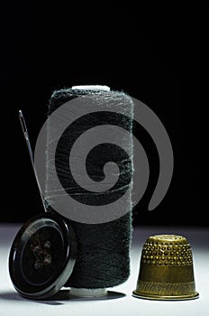 Spool of black thread with a needle, thimble, button