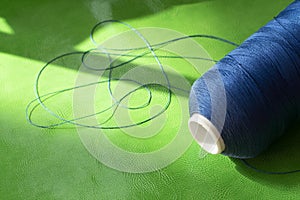 A spool of blue thread on a green leather. Sewing thread. Shoe industry