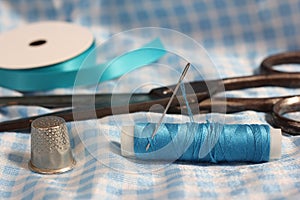 Spool of Blue Thread, Thimble and Needle on Blue and White Fabric