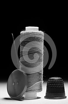 Spool of gray thread with needle thimble and button