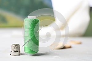 Spool of green sewing thread with needle and thimble on white table, space for text