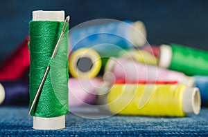 Spool of green thread with a needle on the background of spools of colored threads on a denim, closeup