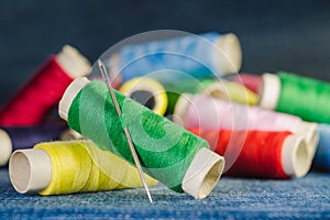 Spool of green thread with a needle on the background of spools of colored threads on a denim fabric